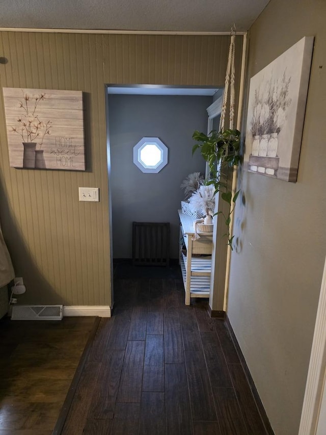 hall featuring baseboards, radiator heating unit, visible vents, and wood finished floors