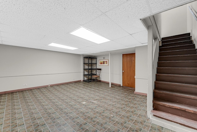 finished basement featuring a paneled ceiling, baseboards, and stairway