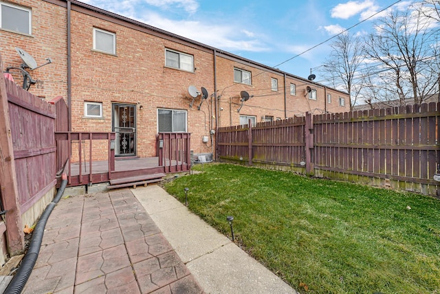 back of property with a deck, a yard, brick siding, and a fenced backyard