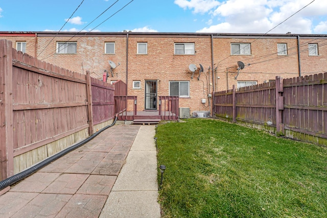 back of property with a fenced backyard, central AC, a lawn, and brick siding