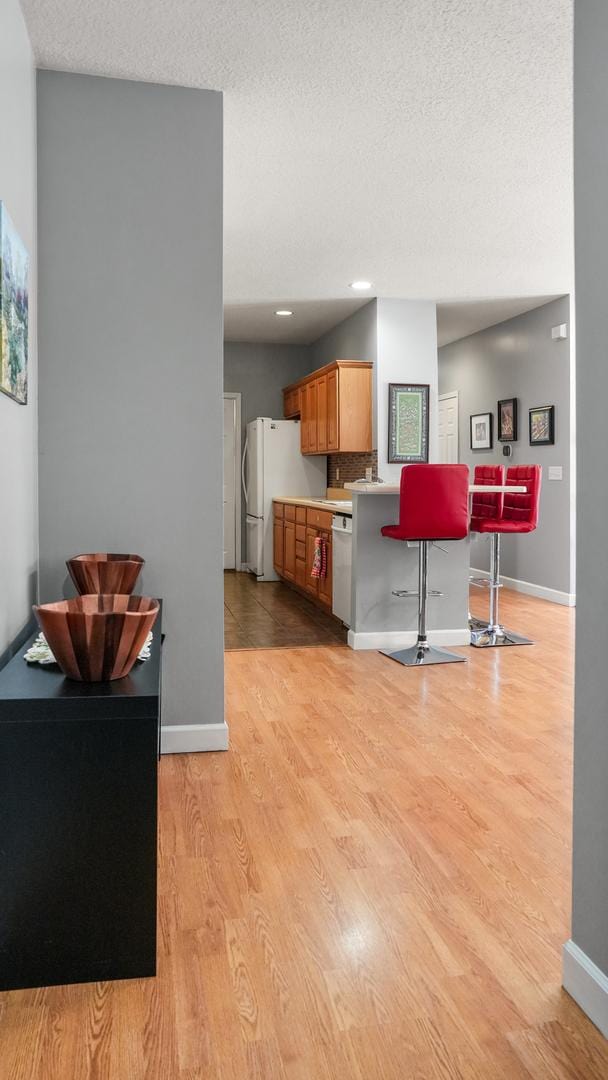 kitchen featuring light wood finished floors, white appliances, a kitchen bar, and baseboards