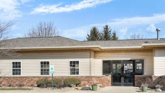 property entrance featuring brick siding, french doors, and a shingled roof