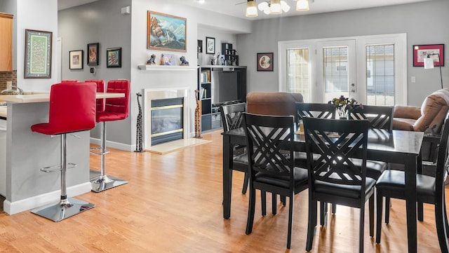 dining room with light wood-style flooring, baseboards, a glass covered fireplace, and french doors