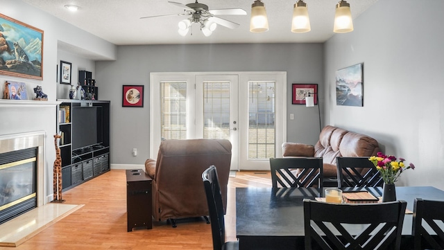 dining area with french doors, light wood-style floors, a fireplace, baseboards, and ceiling fan