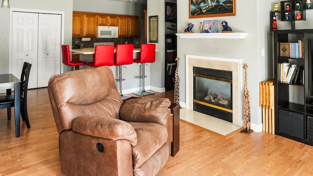 living room with a glass covered fireplace, baseboards, and light wood-type flooring