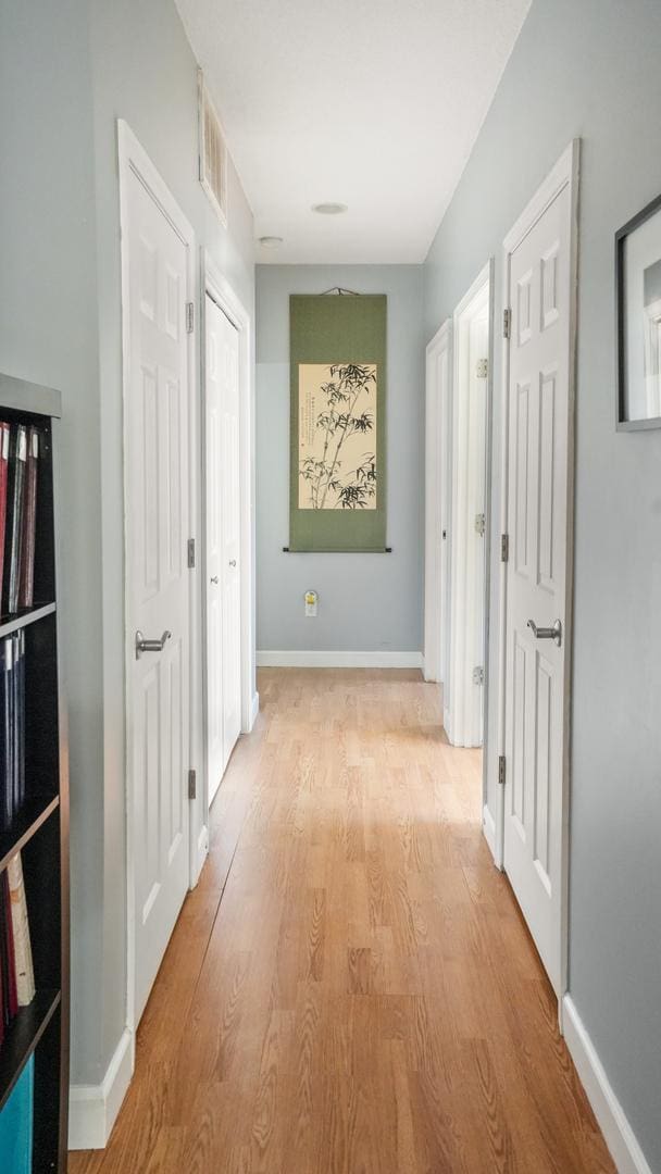 corridor with light wood-type flooring, baseboards, and visible vents