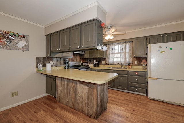 kitchen featuring stainless steel gas range oven, a sink, freestanding refrigerator, a peninsula, and light countertops