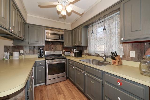 kitchen featuring gray cabinetry, a sink, stainless steel appliances, crown molding, and light countertops