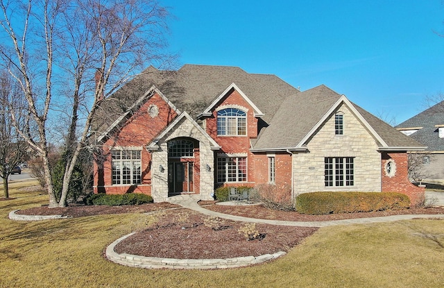 view of front facade featuring a shingled roof, stone siding, brick siding, and a front lawn