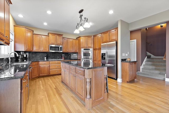 kitchen featuring appliances with stainless steel finishes, a sink, light wood-style floors, and a center island