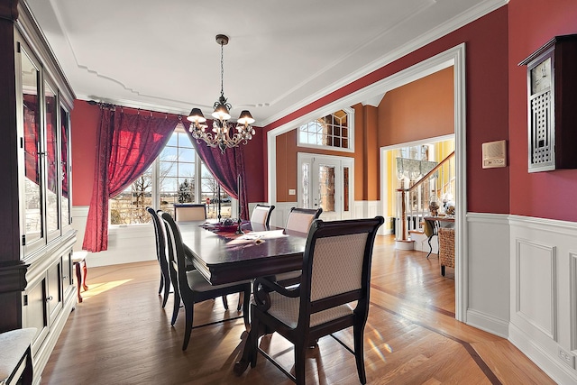 dining space with a wainscoted wall, a notable chandelier, ornamental molding, and wood finished floors