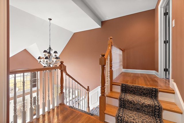 stairway with vaulted ceiling, wood finished floors, and a chandelier