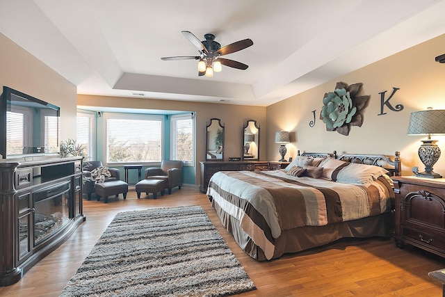 bedroom featuring ceiling fan, a raised ceiling, and wood finished floors