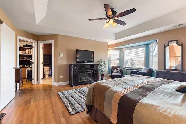 bedroom with a raised ceiling, visible vents, light wood-style flooring, a glass covered fireplace, and baseboards