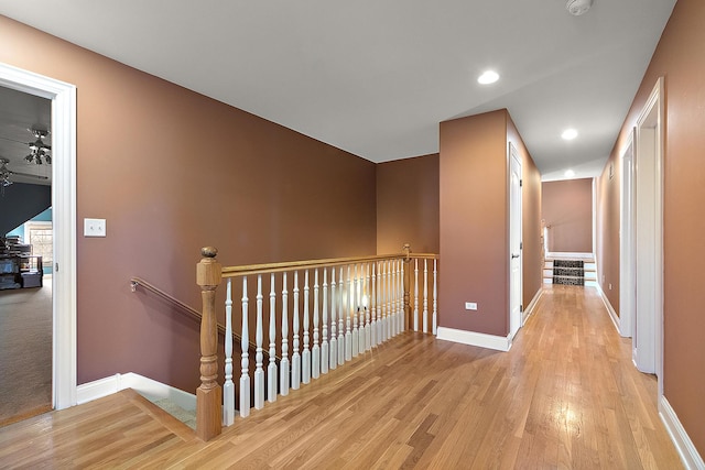 corridor featuring light wood-type flooring, recessed lighting, baseboards, and an upstairs landing