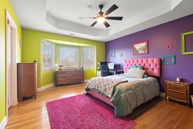 bedroom featuring a ceiling fan, visible vents, baseboards, light wood-type flooring, and a raised ceiling