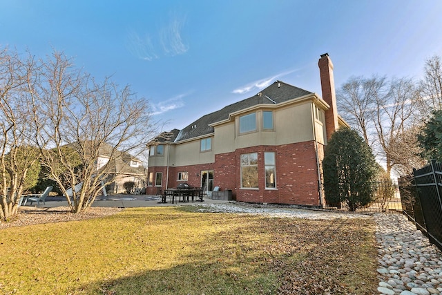 rear view of property featuring a patio, brick siding, fence, a lawn, and a chimney