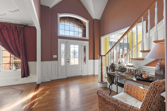 entryway featuring a wainscoted wall, stairway, wood finished floors, vaulted ceiling, and a decorative wall