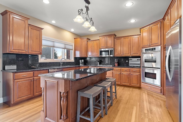 kitchen with stainless steel appliances, light wood-style flooring, decorative backsplash, brown cabinetry, and a sink