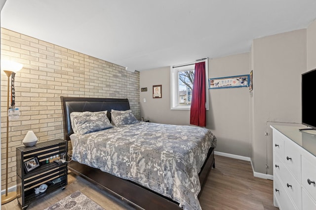 bedroom with brick wall, baseboards, and wood finished floors