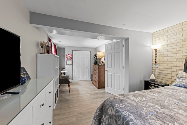 bedroom with a closet, light wood-style flooring, and brick wall