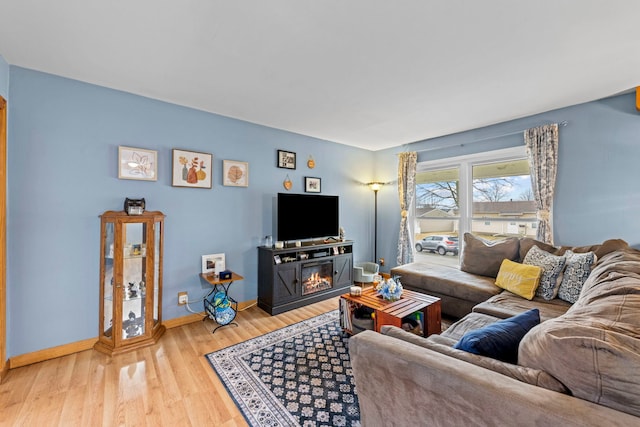 living area with a glass covered fireplace, baseboards, and wood finished floors