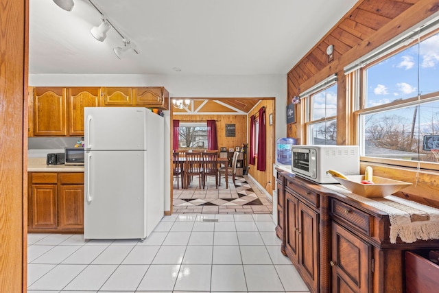 kitchen with brown cabinets, light tile patterned floors, light countertops, freestanding refrigerator, and wooden walls