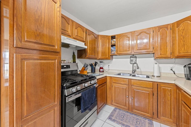 kitchen with brown cabinets, stainless steel gas range, light countertops, under cabinet range hood, and a sink