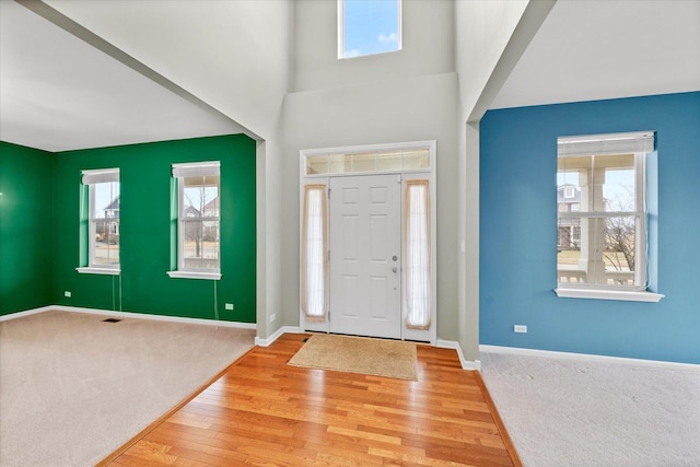 foyer featuring carpet floors, hardwood / wood-style floors, a high ceiling, and baseboards