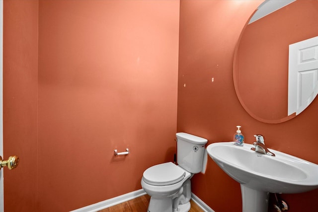 half bathroom featuring baseboards, a sink, toilet, and wood finished floors