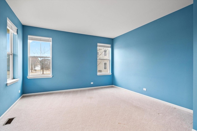 carpeted empty room featuring visible vents, a wealth of natural light, and baseboards