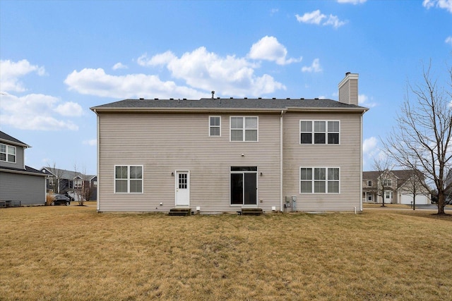 rear view of house with entry steps, a yard, and a chimney