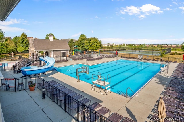 pool featuring a water slide, a patio area, and fence