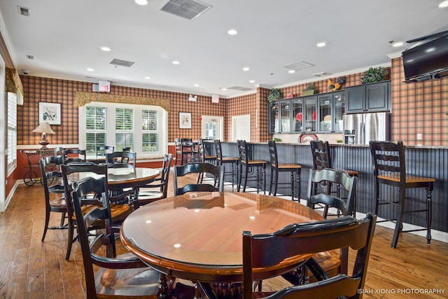 dining room featuring a dry bar, wallpapered walls, visible vents, and wood finished floors