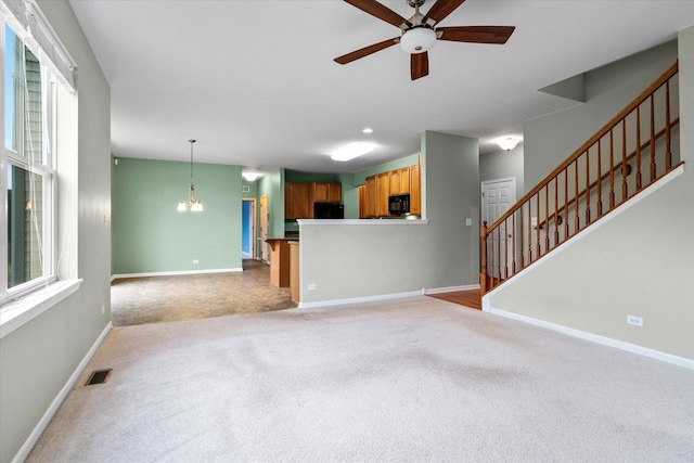 unfurnished living room featuring light colored carpet, visible vents, stairway, baseboards, and ceiling fan with notable chandelier