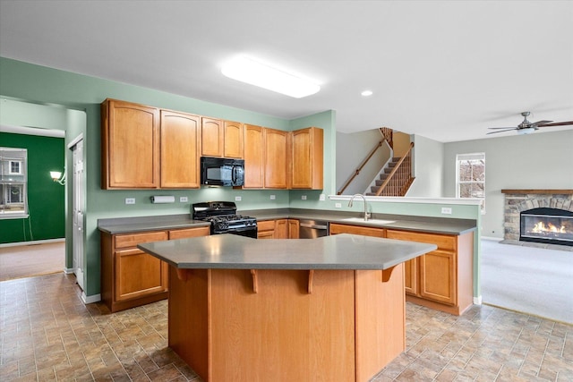 kitchen featuring baseboards, a peninsula, black appliances, a fireplace, and a sink