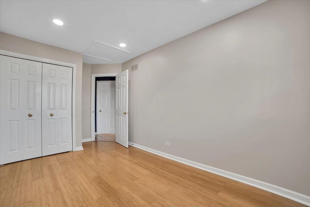 unfurnished bedroom with a closet, visible vents, attic access, light wood-type flooring, and baseboards