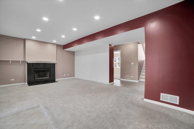 unfurnished living room featuring recessed lighting, light colored carpet, a fireplace with flush hearth, visible vents, and stairway