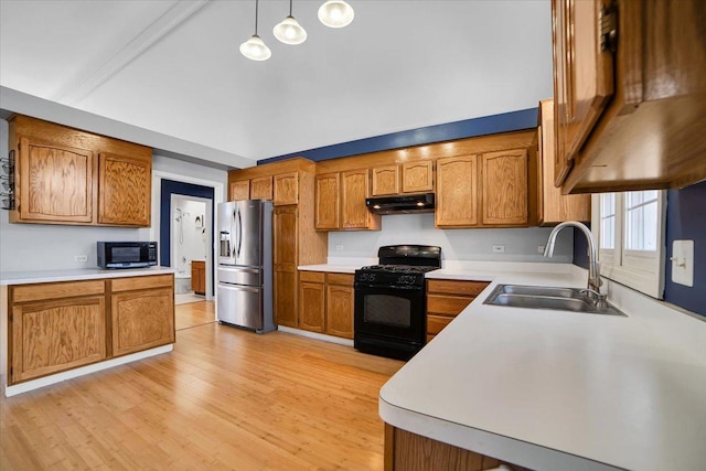 kitchen featuring brown cabinets, gas stove, a sink, stainless steel fridge, and under cabinet range hood