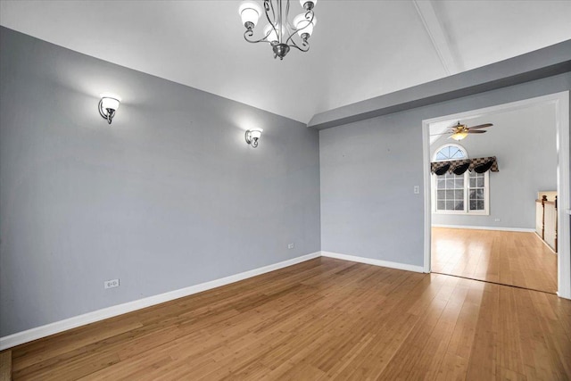 empty room featuring vaulted ceiling, ceiling fan with notable chandelier, hardwood / wood-style flooring, and baseboards