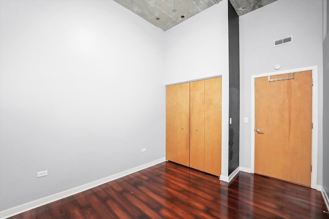 unfurnished bedroom with baseboards, visible vents, wood finished floors, a high ceiling, and a closet