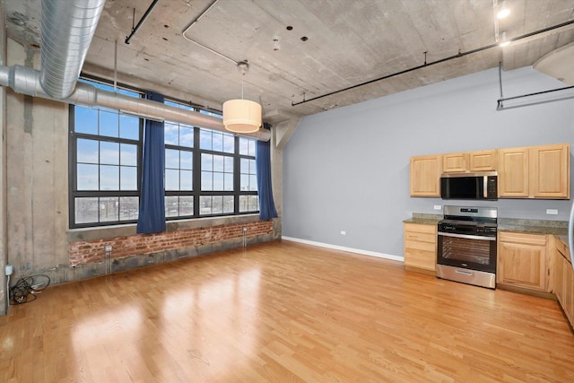 kitchen featuring a towering ceiling, appliances with stainless steel finishes, light wood-style floors, light brown cabinets, and baseboards