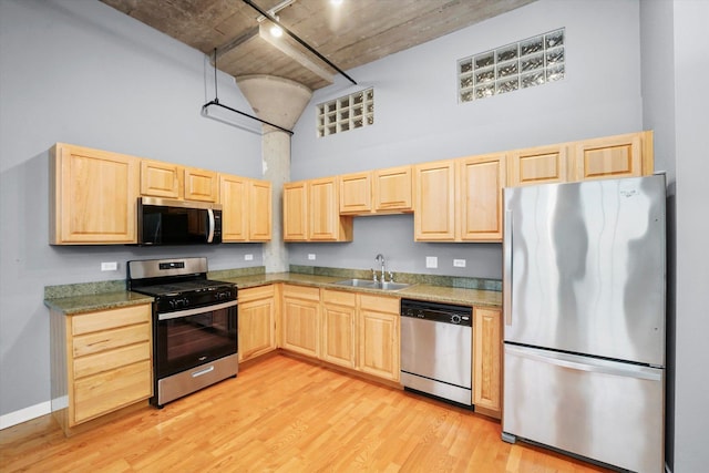 kitchen featuring appliances with stainless steel finishes, a sink, a high ceiling, and light brown cabinetry