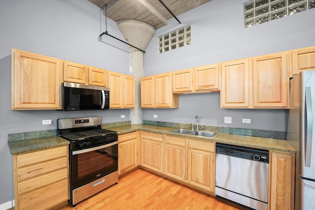 kitchen featuring a high ceiling, light brown cabinets, appliances with stainless steel finishes, and a sink