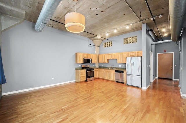 kitchen with stainless steel appliances, a towering ceiling, light brown cabinetry, light wood-style floors, and a sink