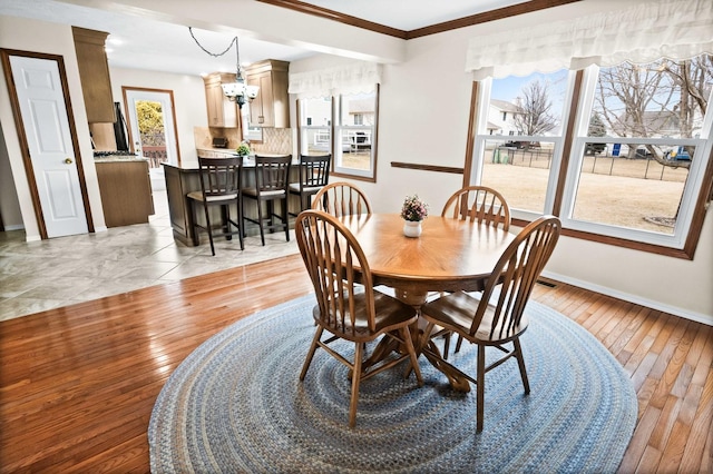 dining space featuring light wood finished floors, baseboards, a chandelier, and ornamental molding