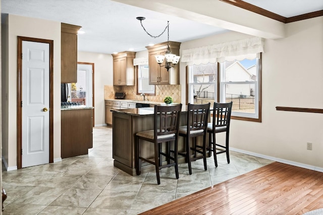 kitchen featuring baseboards, a breakfast bar, backsplash, a notable chandelier, and a sink