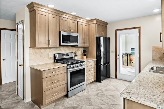 kitchen with light stone counters, recessed lighting, stainless steel appliances, a sink, and backsplash