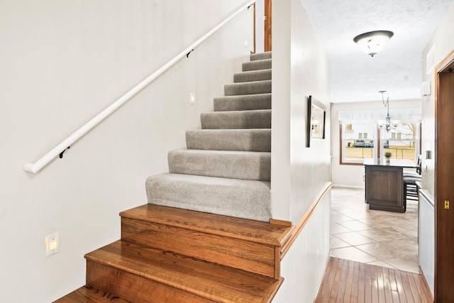 staircase with a chandelier, a textured ceiling, and tile patterned flooring