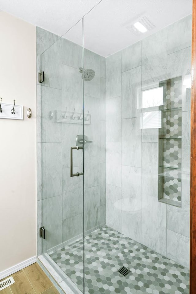 bathroom featuring a stall shower, visible vents, baseboards, and wood finished floors